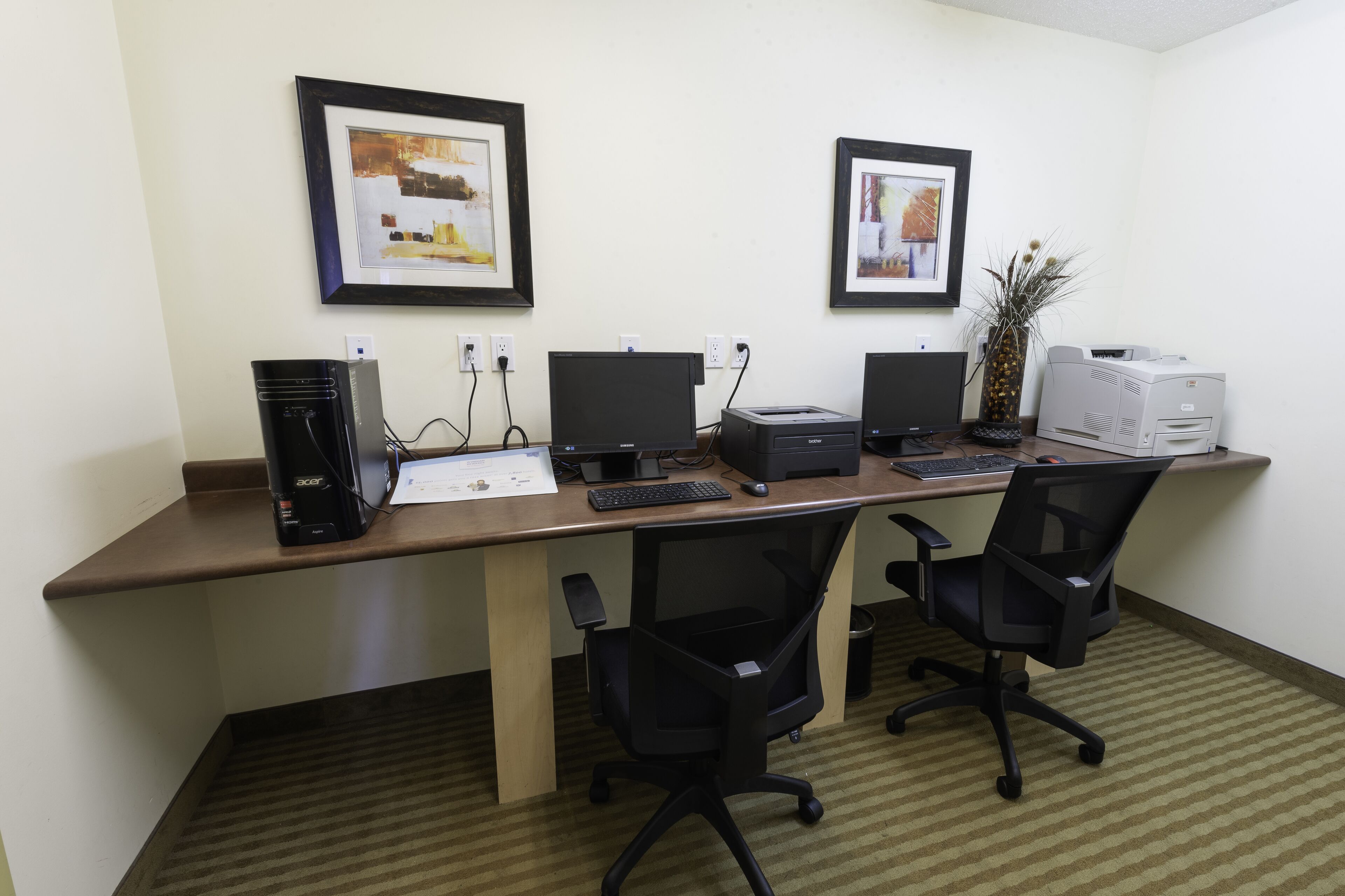 Un espacio de trabajo con dos escritorios, computadoras, sillas e imágenes enmarcadas en la pared.