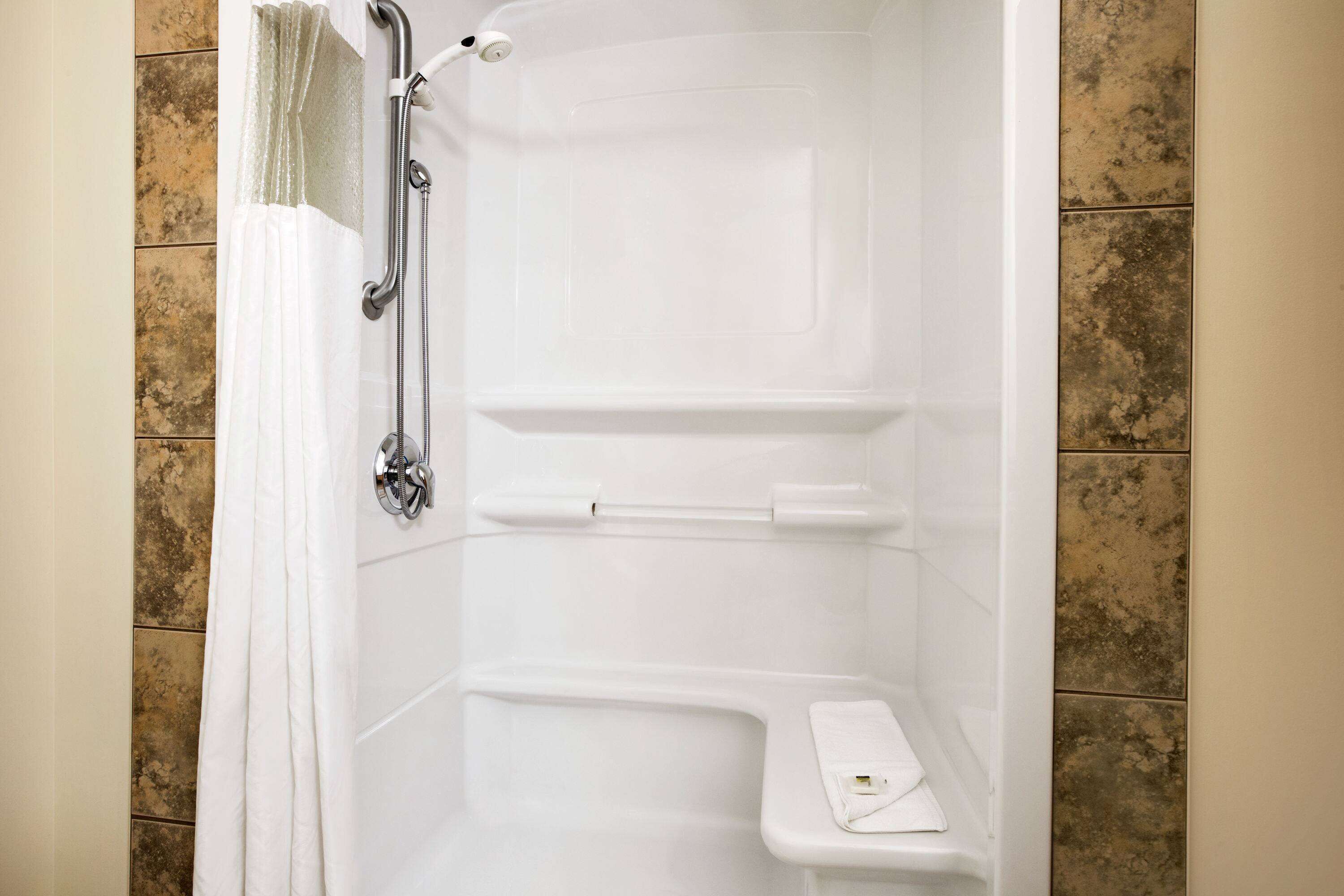 A walk-in shower with a handheld showerhead, a towel rack, and a shelf.