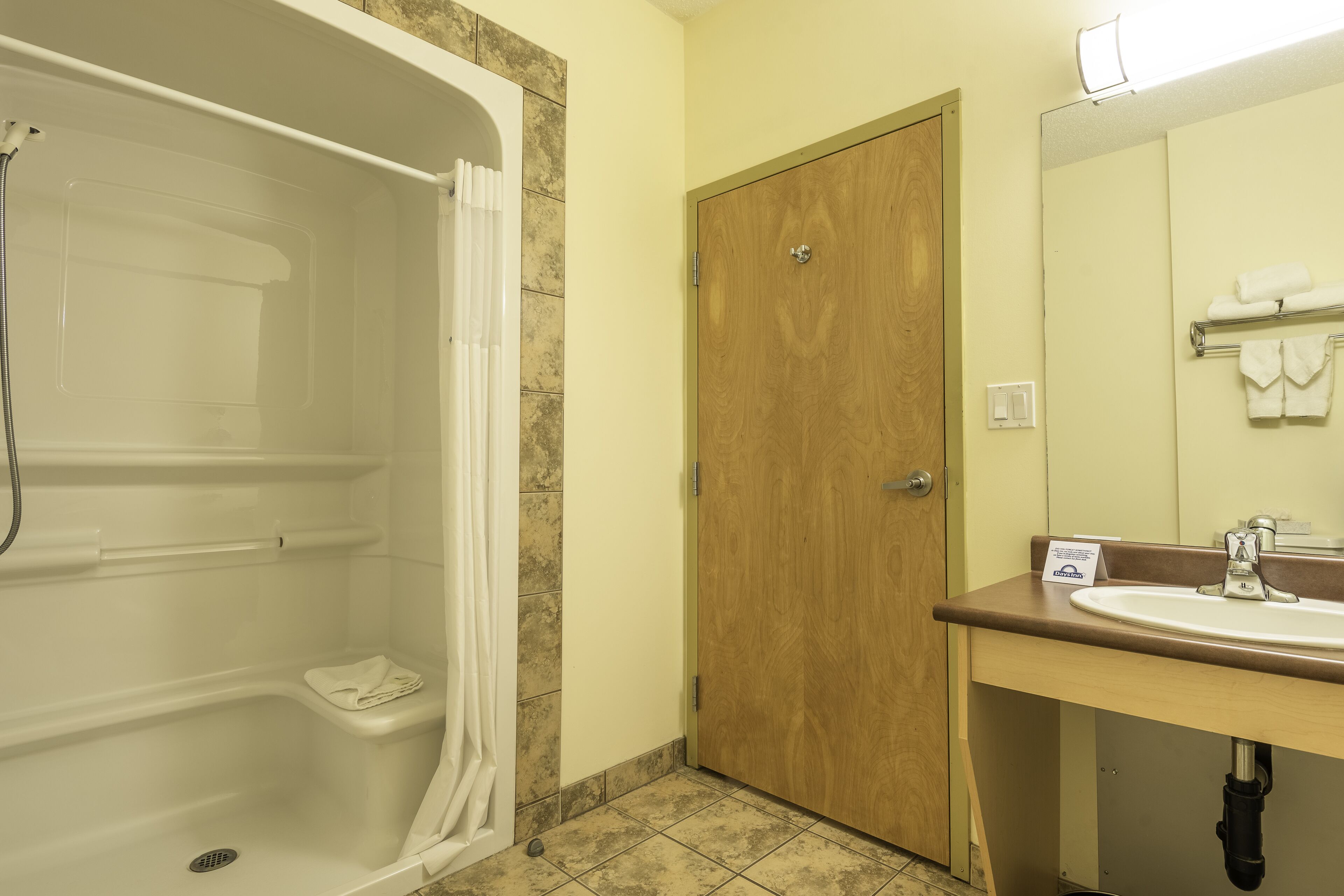 A bathroom with a bathtub, a wooden door, a sink with a mirror, and a towel rack.