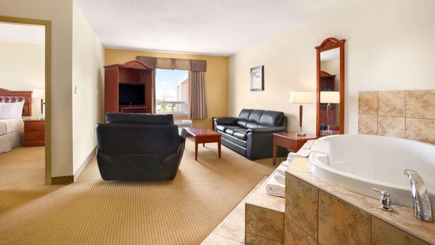 Habitación de hotel con sala de estar, sofá, televisor, bañera grande y espejo.