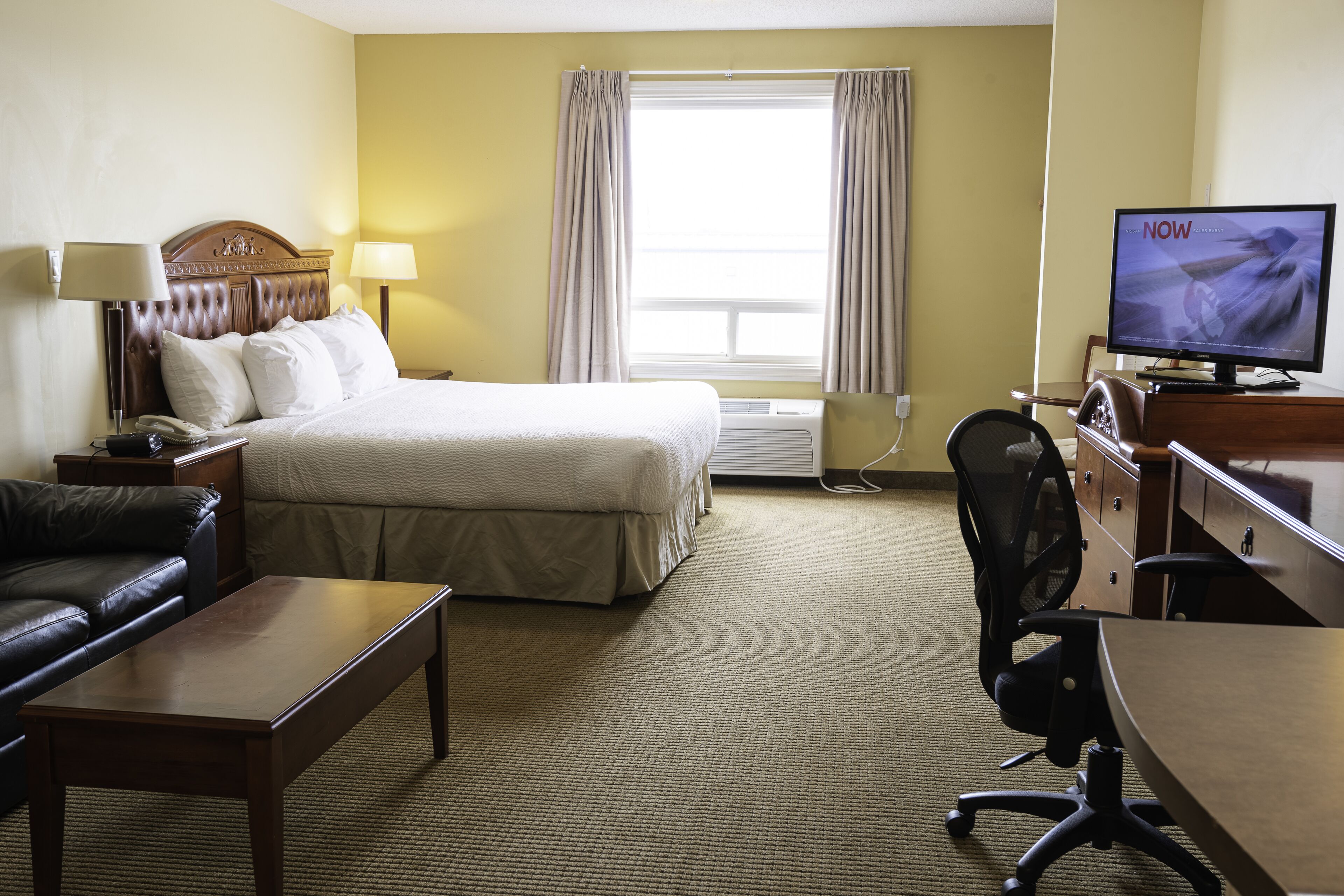 Une chambre d’hôtel comprenant un lit, un bureau, une chaise, un téléviseur et un canapé en cuir.