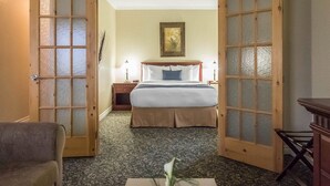 Una habitación de hotel con una cama, una mesita de noche, una lámpara, un cuadro en la pared y una puerta con paneles de vidrio esmerilado.