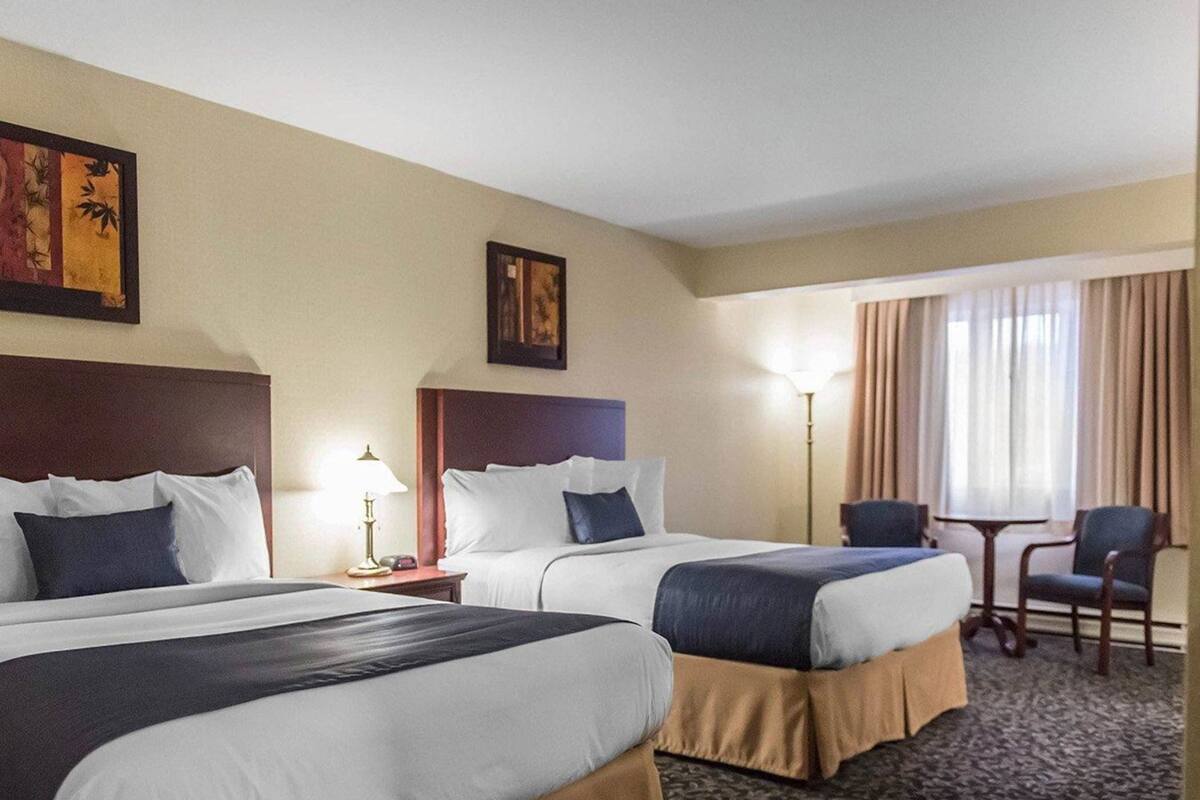 A hotel room with two beds, a desk, a chair, and a lamp.