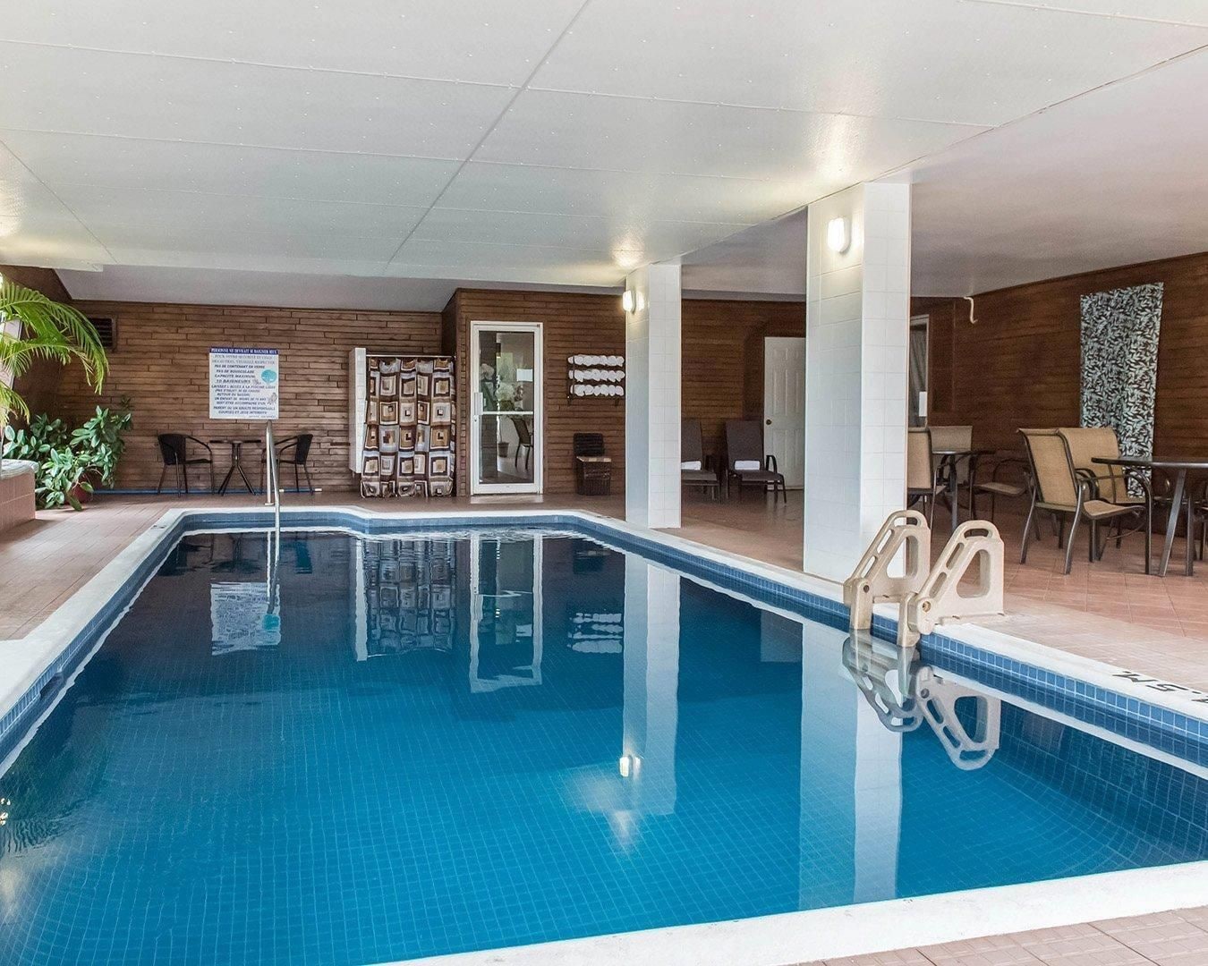 An indoor swimming pool with a clear view of the pool area, a seating area with chairs and tables, and a wooden wall with a door.