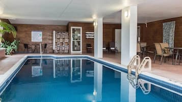 An indoor swimming pool with a clear view of the pool area, a seating area with chairs and tables, and a wooden wall with a door.