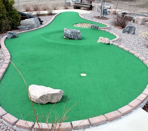 Un campo de mini golf con césped artificial verde, varios obstáculos y una pelota blanca.