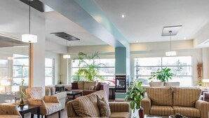 Un amplio hall de hotel con varias zonas de estar, ventanas grandes y plantas de interior.