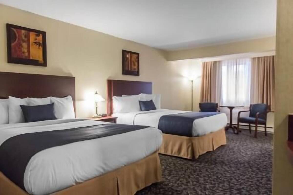 A hotel room with two beds, a small table, a chair, and a lamp.