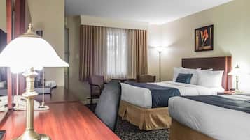 A hotel room with two beds, a desk with a lamp, a chair, a desk lamp, a painting on the wall, and a window with curtains.