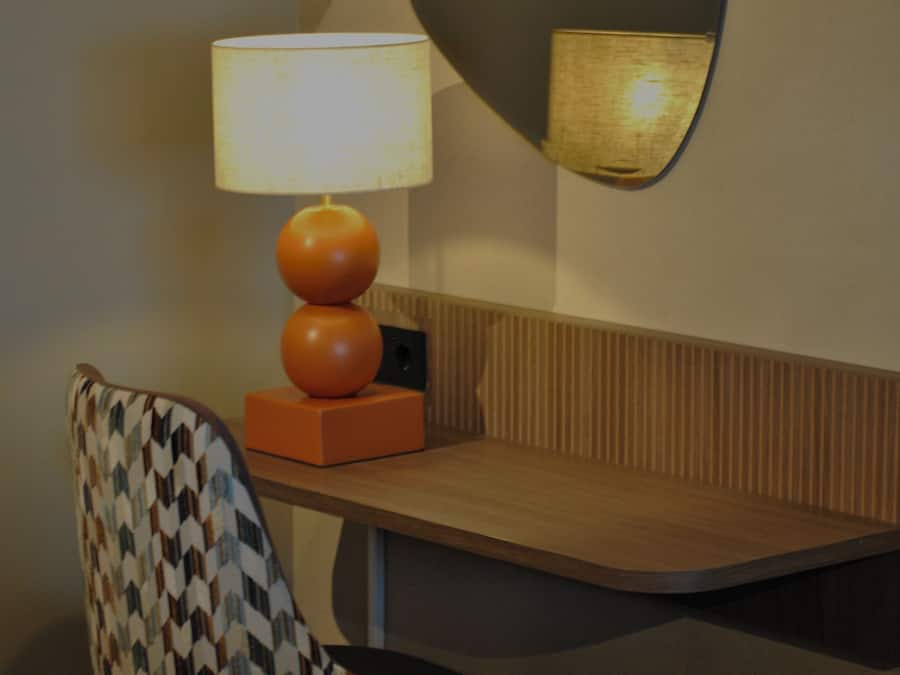 Una habitación de hotel con cama, una silla, una mesa, una lámpara y un espejo fijado a la pared.
