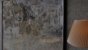 Un comedor con una mesa dispuesta para dos personas, un cuadro abstracto colgado en la pared y una lámpara.