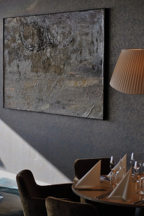 A dining area with a table set for two, a wall-mounted abstract painting, and a lamp. - Strand Öland (Borgholm)