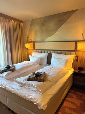 A hotel room with a large bed, two bedside tables, a headboard with a textured panel, and a wall-mounted lamp. - Strand Öland (Borgholm)