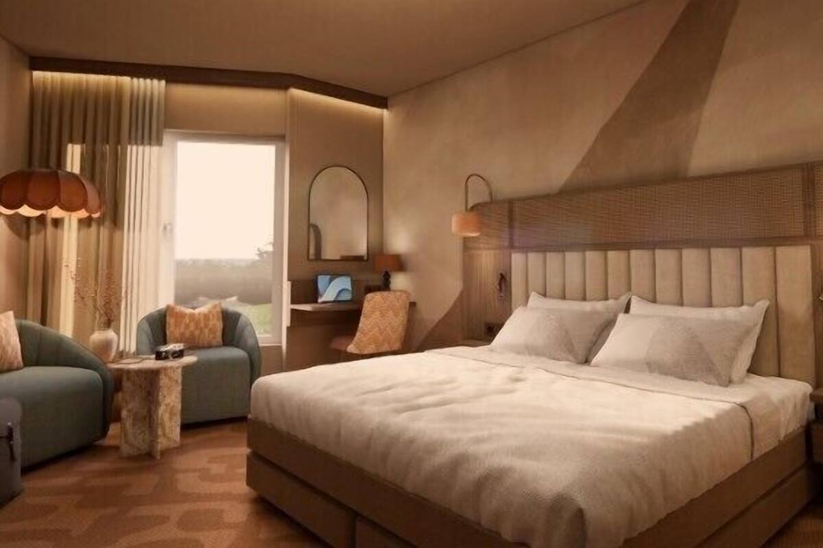 Ein Hotelzimmer mit einem großen Bett, zwei Sesseln, einem kleinen Tisch, einem Nachttisch, einer Lampe und einem Fenster mit Vorhängen.