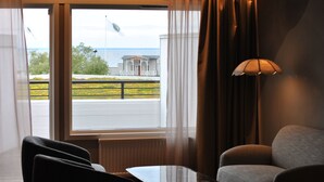 Habitación de hotel con vista a un edificio y una bandera, una mesa, un sofá y una lámpara.