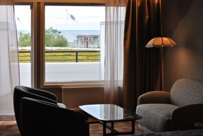 A hotel room with a view of a building and a flag, a table, a sofa, and a lamp. - Strand Öland (Borgholm)