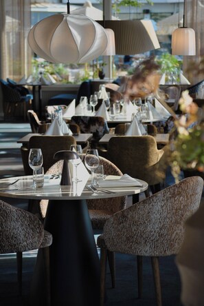 A restaurant interior with round tables, chairs, and a modern chandelier. - Strand Öland (Borgholm)