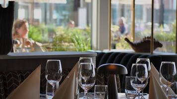 Una mesa de comedor preparada con varias copas de vino, un salero y cubiertos, con vistas al exterior a través de una ventana.