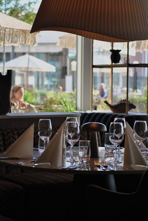 Una mesa de comedor preparada con varias copas de vino, un salero y cubiertos, con vistas al exterior a través de una ventana.