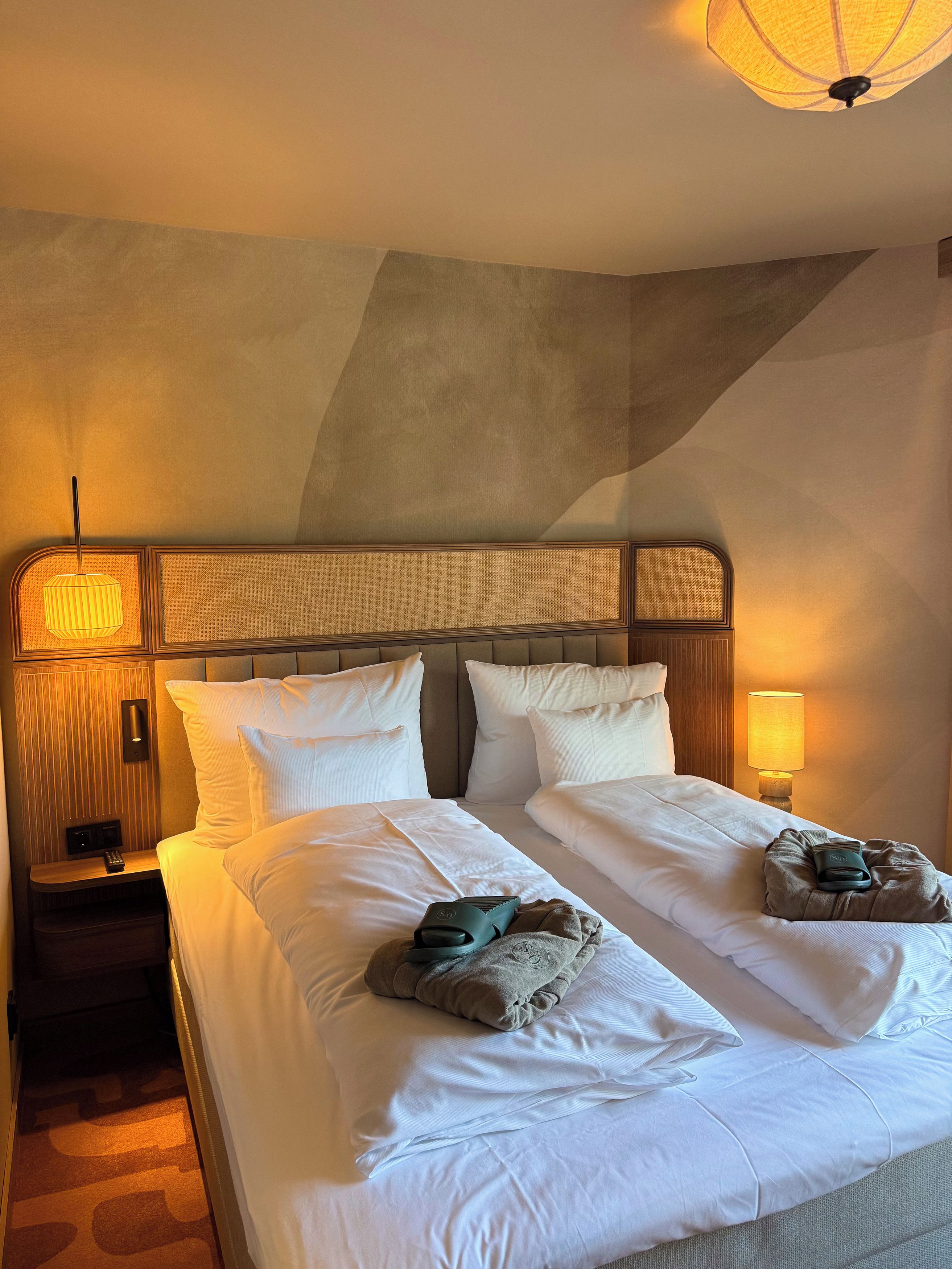 Una habitación de hotel con una cama grande, dos mesitas de noche, una lámpara de pared y una luz en el techo.