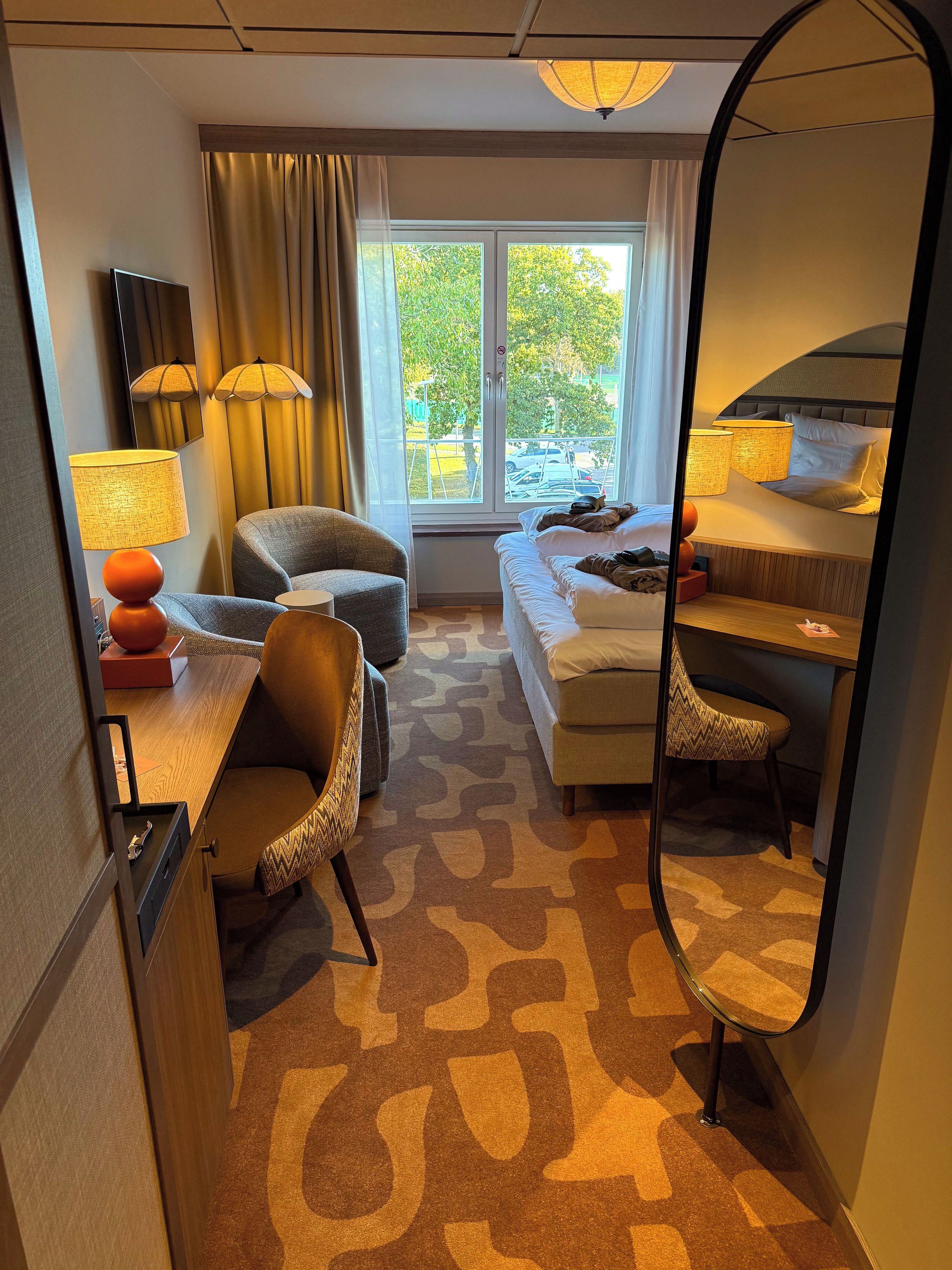 Una habitación de hotel con cama, escritorio, silla, sofá y un espejo grande.
