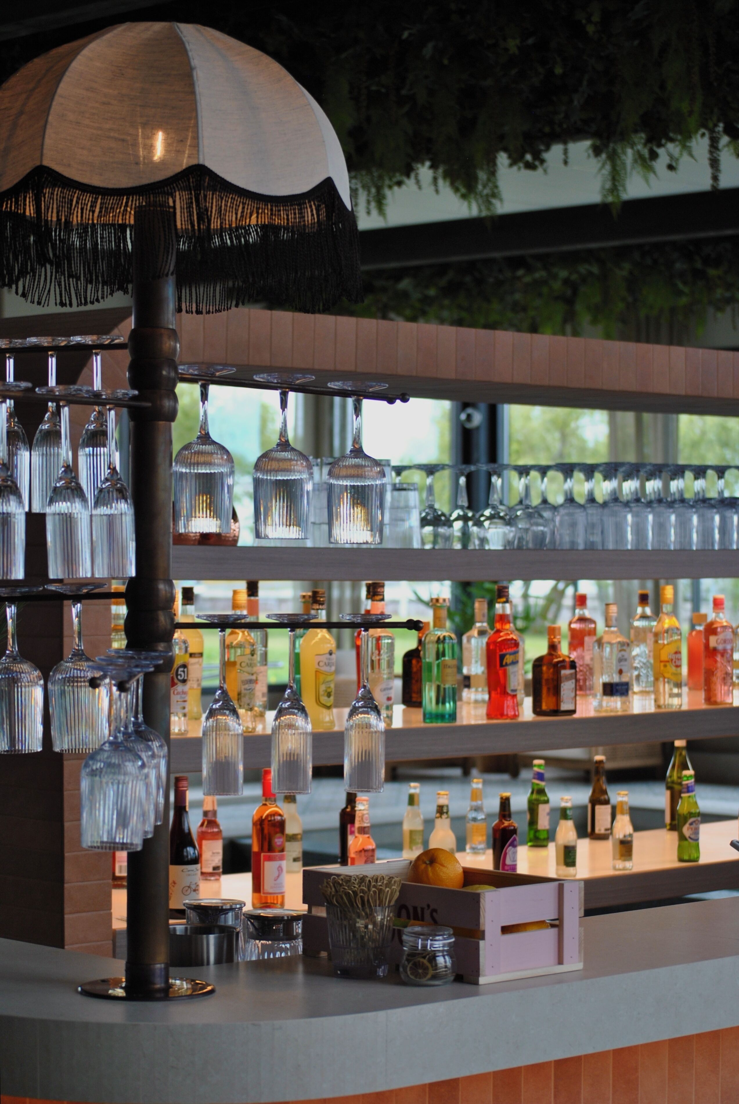 A bar area with multiple hanging glassware, a variety of bottles, and a decorative umbrella.
