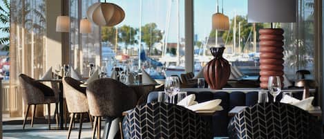 A restaurant with a view of boats, modern furniture, and pendant lighting.