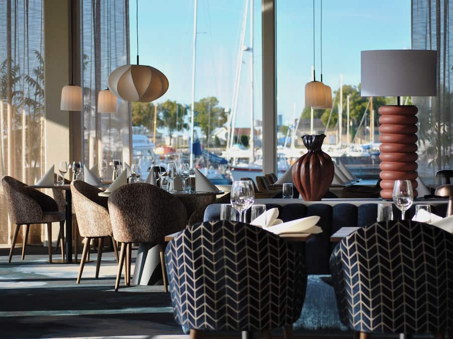 En restaurant med udsigt til både, moderne møbler og hængende lamper.