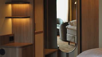 Habitación de hotel con cama, espejo que refleja un sofá y cortinas, y un armario de madera.