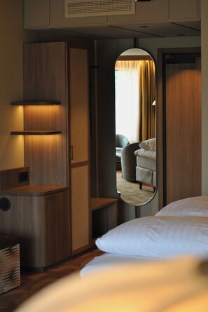 Habitación de hotel con cama, espejo que refleja un sofá y cortinas, y un armario de madera.