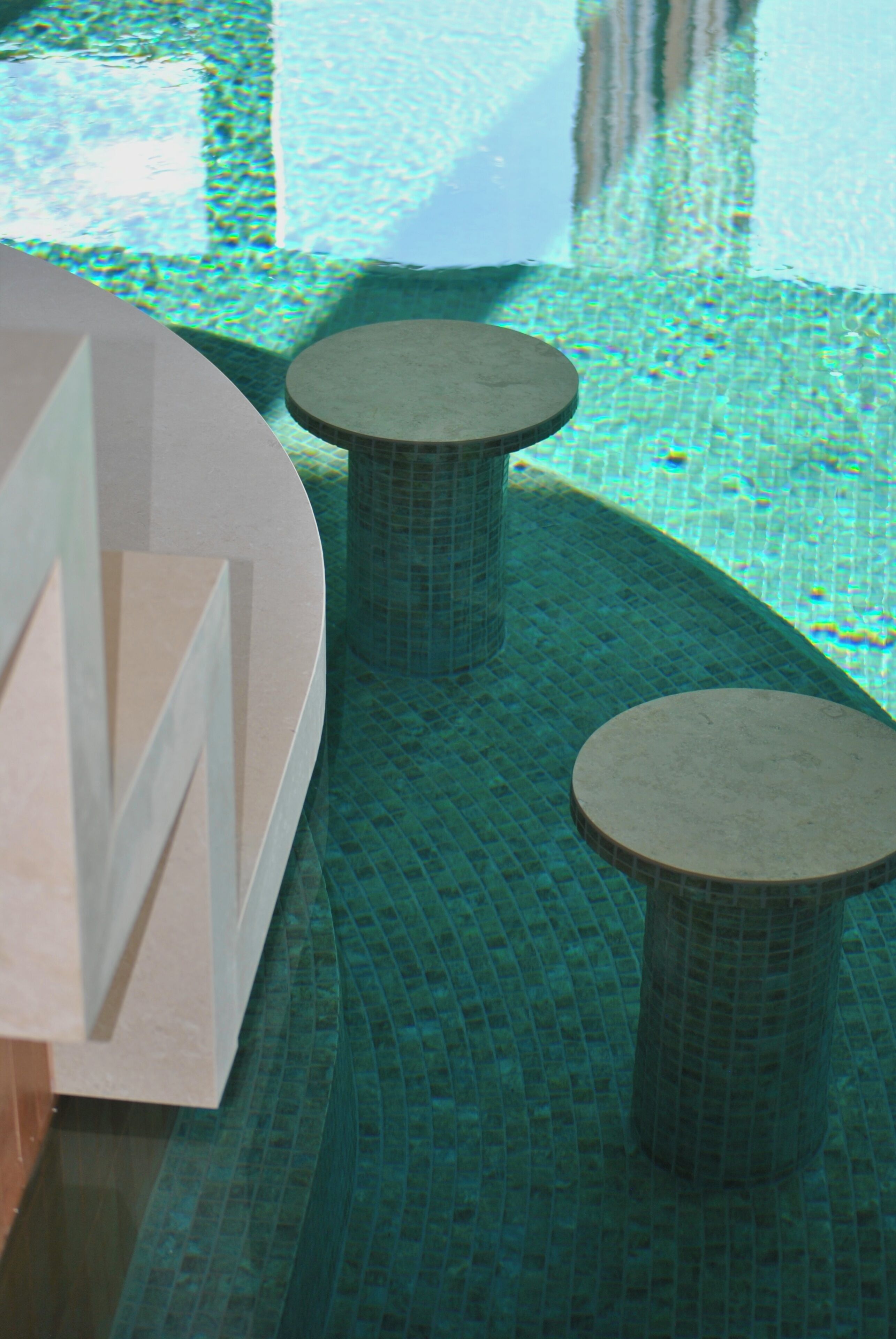 Un espace piscine doté d’un sol carrelé et de deux tables rondes.