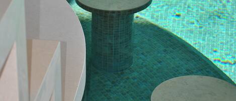 Un espace piscine doté d’un sol carrelé et de deux tables rondes.