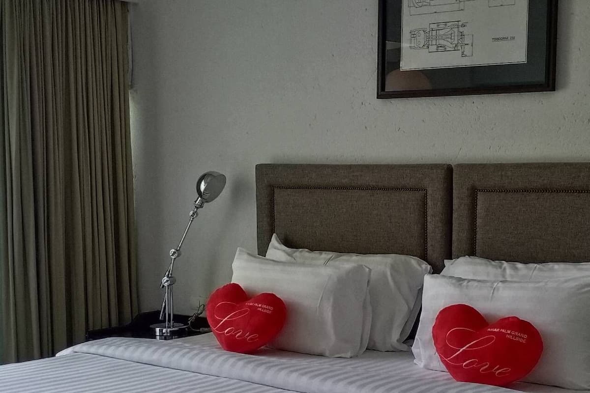 Habitación de hotel con cama, dos almohadas, lámpara de noche y un dibujo arquitectónico enmarcado en la pared.
