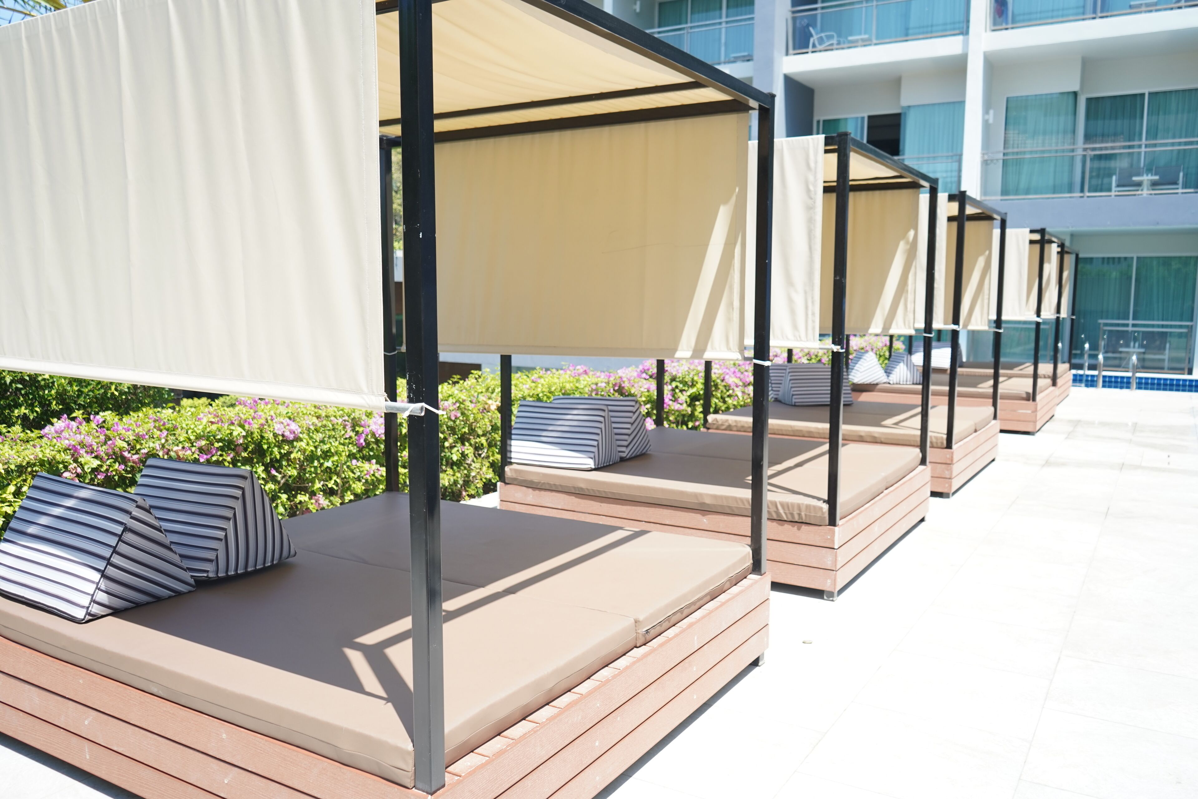 Outdoor seating areas with cushioned benches and privacy screens, set against a backdrop of a modern building and lush greenery.
