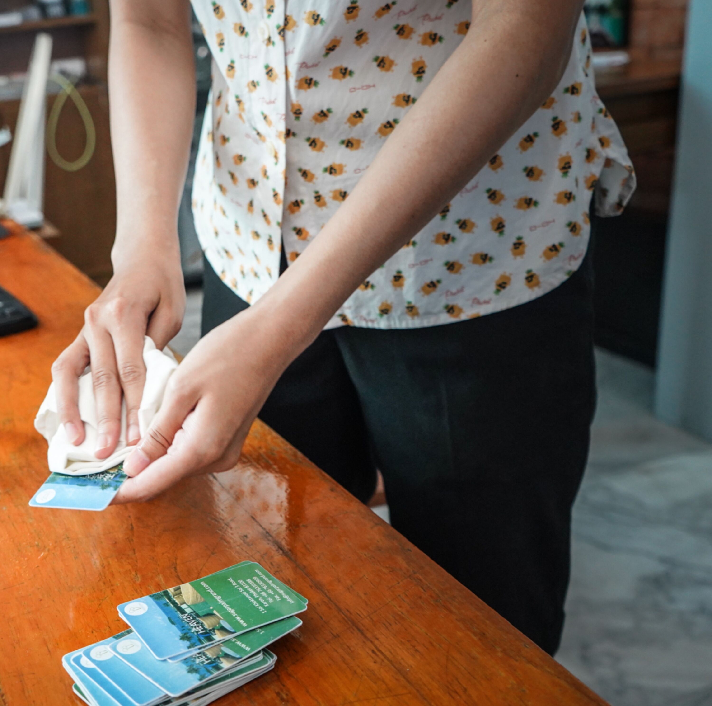 A person wiping a card on a wooden table with a cloth.