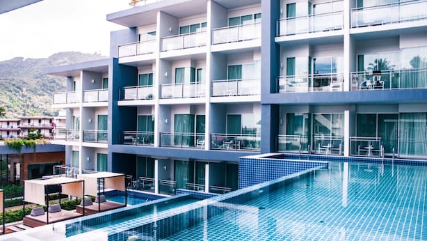 A modern hotel with a large swimming pool, multiple balconies, and a view of the surrounding landscape. - Sugar Palm Grand Hillside (Karon)