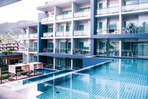 A modern hotel with a large swimming pool, multiple balconies, and a view of the surrounding landscape. - Sugar Palm Grand Hillside (Karon)