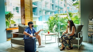 A modern hotel lobby with a seating area, a reception desk, and a large window offering a view of the building's exterior. - Sugar Palm Grand Hillside (Karon)