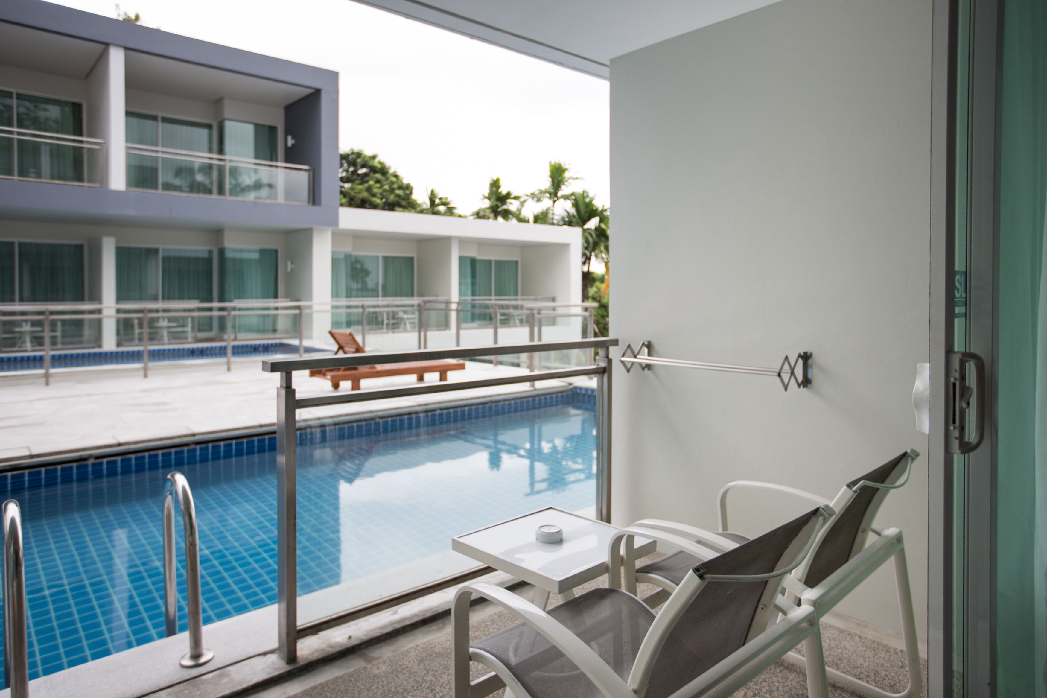 A modern hotel room with a balcony overlooking a swimming pool, a dining area, and a view of the building's exterior.