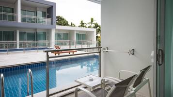 A modern hotel room with a balcony overlooking a swimming pool, a dining area, and a view of the building's exterior.