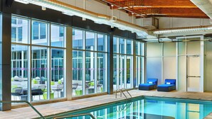 A modern indoor swimming pool with clear glass walls, blue lounge chairs, and a view of the outdoor area. - Aloft by Marriott Denver Airport at Gateway Park (Aurora)