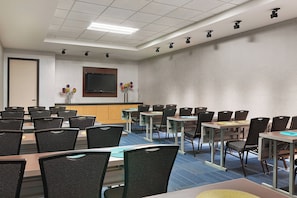A conference room with multiple tables and chairs, a flat-screen TV mounted on the wall, and a small bar area. - Aloft by Marriott Denver Airport at Gateway Park (Aurora)