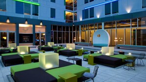 A modern outdoor seating area with multiple tables and chairs, large windows, and a distinctive curved white wall. - Aloft by Marriott Denver Airport at Gateway Park (Aurora)