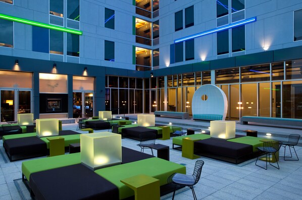 A modern outdoor seating area with multiple tables and chairs, large windows, and a distinctive curved white wall. - Aloft by Marriott Denver Airport at Gateway Park (Aurora)