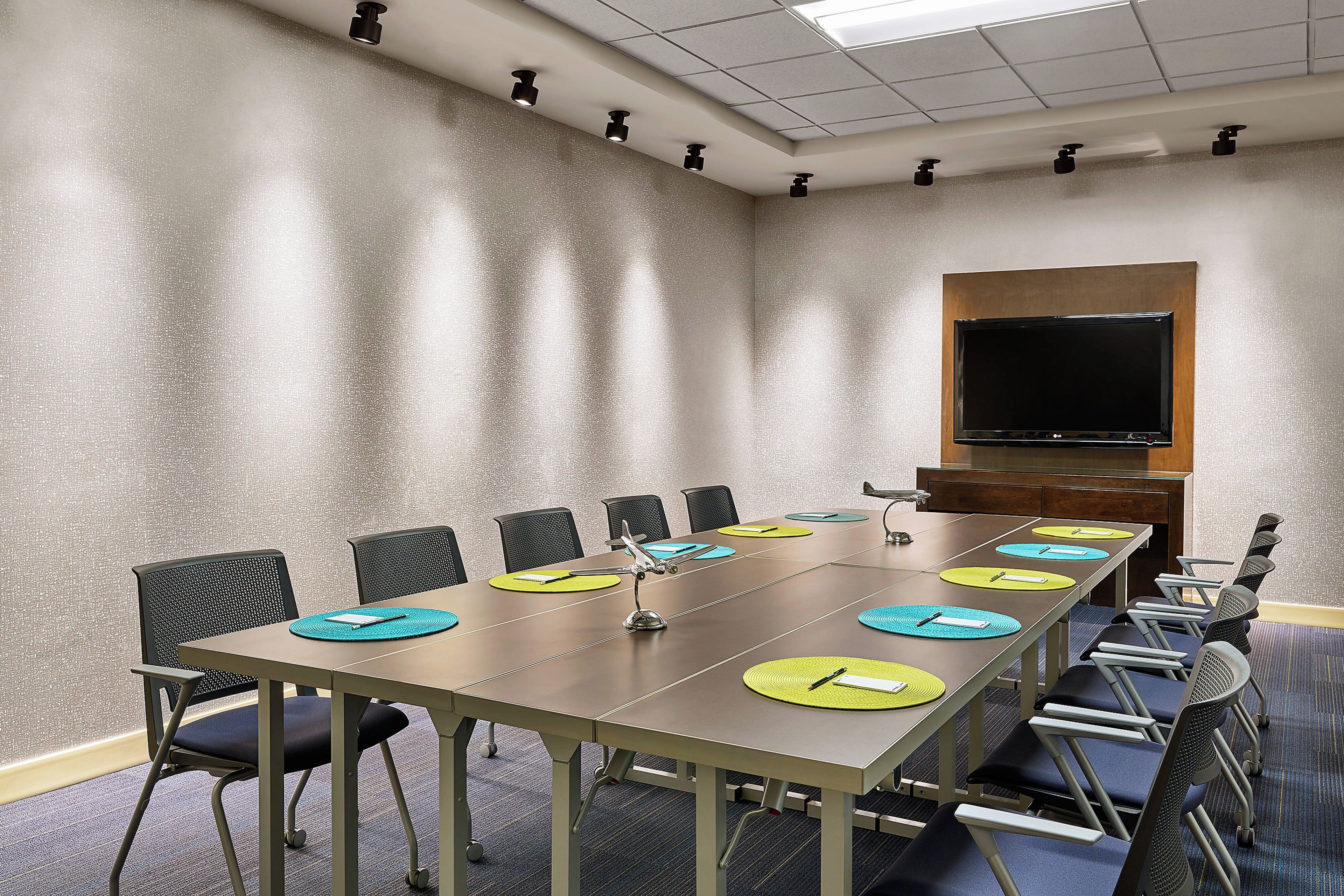 A conference room with a long table, chairs, a projector screen, and a flat-screen TV.
