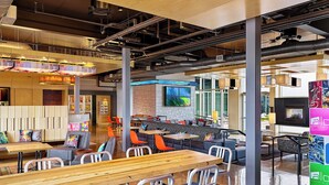 A modern restaurant with high ceilings, exposed ductwork, and a mix of seating options including tables and booths. - Aloft by Marriott Denver Airport at Gateway Park (Aurora)