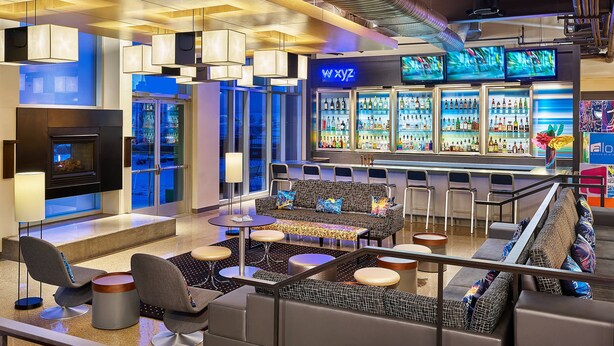 A modern bar area with seating, a bar counter, and a large refrigerator stocked with beverages. - Aloft by Marriott Denver Airport at Gateway Park (Aurora)
