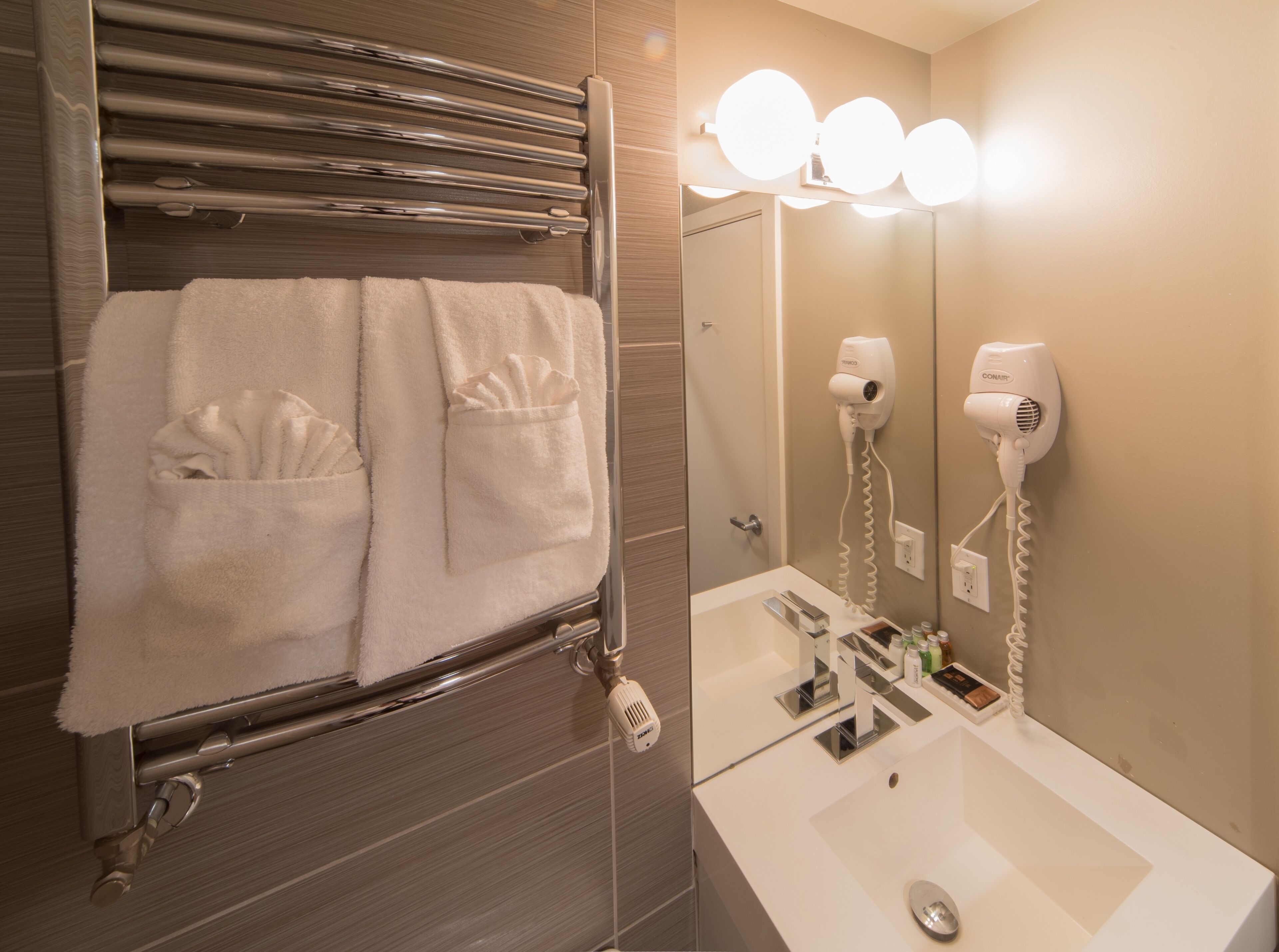 A bathroom with a towel rack holding two towels, a hairdryer, and a mirror with lights.