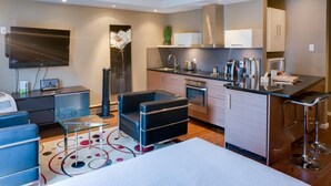 A modern kitchen with a flat-screen TV, a coffee machine, and a bar area with stools. - Nuvo Hotel & Suites (Calgary)