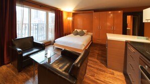 A modern hotel room with a bed, a glass coffee table, a leather sofa, wooden cabinets, and a view of the city. - Nuvo Hotel & Suites (Calgary)